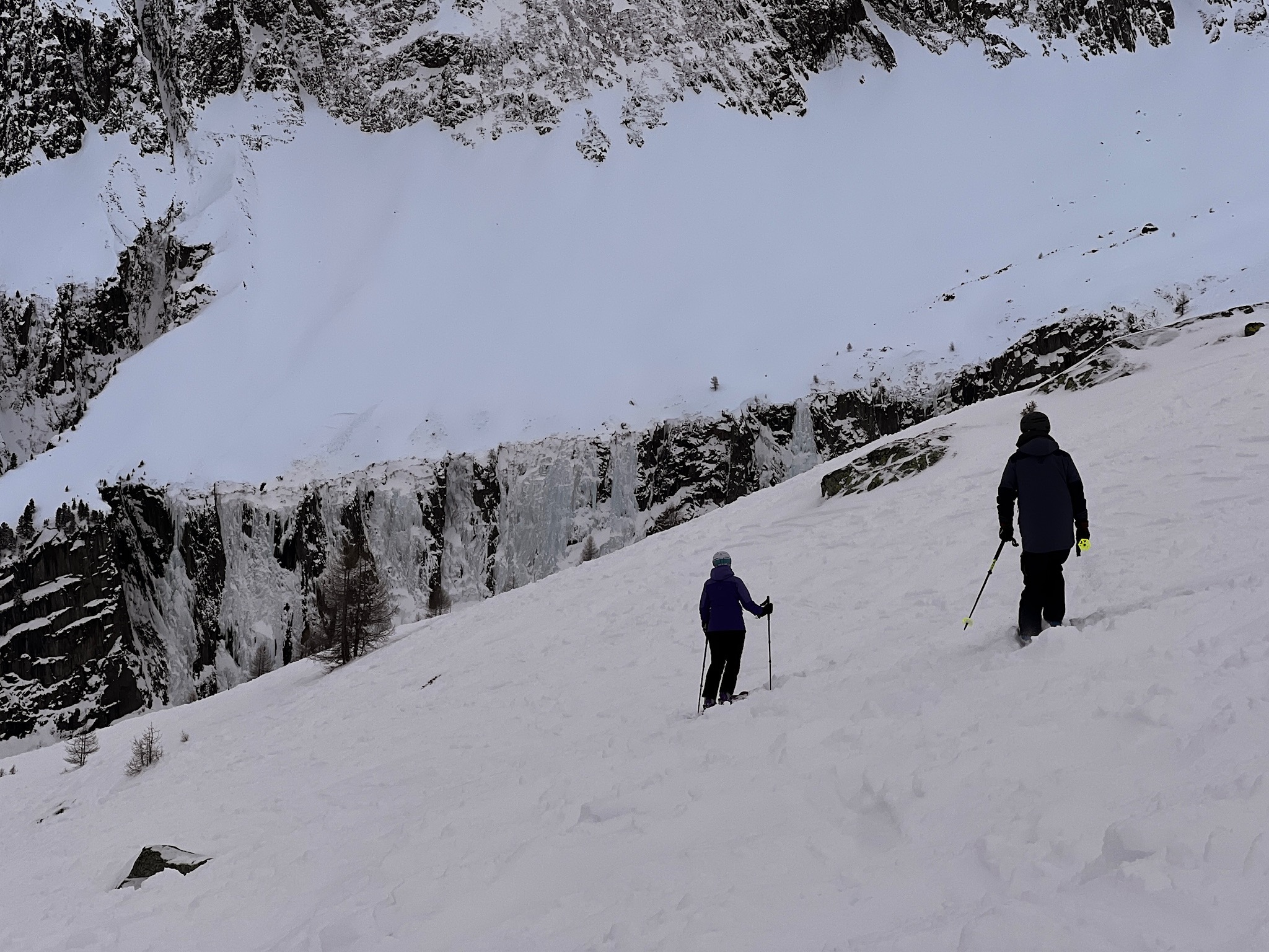 Two skiers on a snowy slope with a frozen icefall above